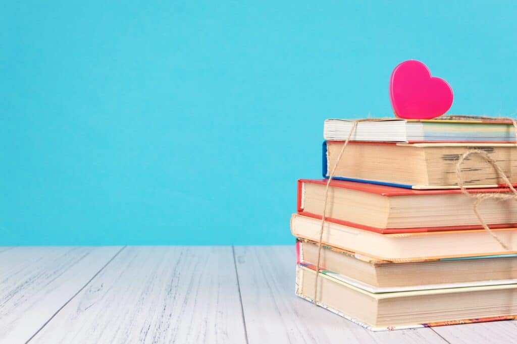 Stack of books and pink heart. Books with jute ribbon bow as gift on blue background. Education